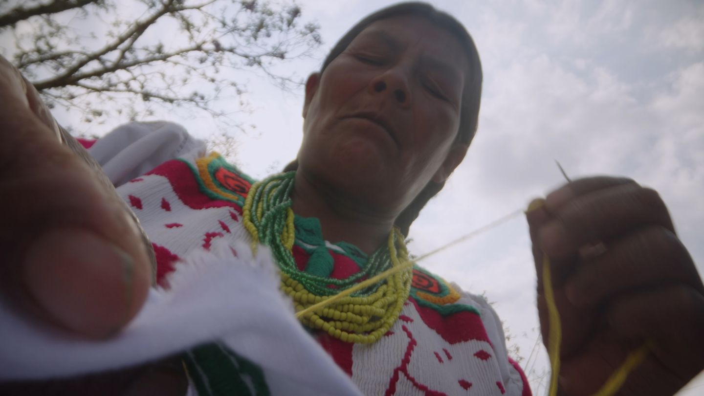 Una mujer borda al atardecer, con collares de cuentas verdes.