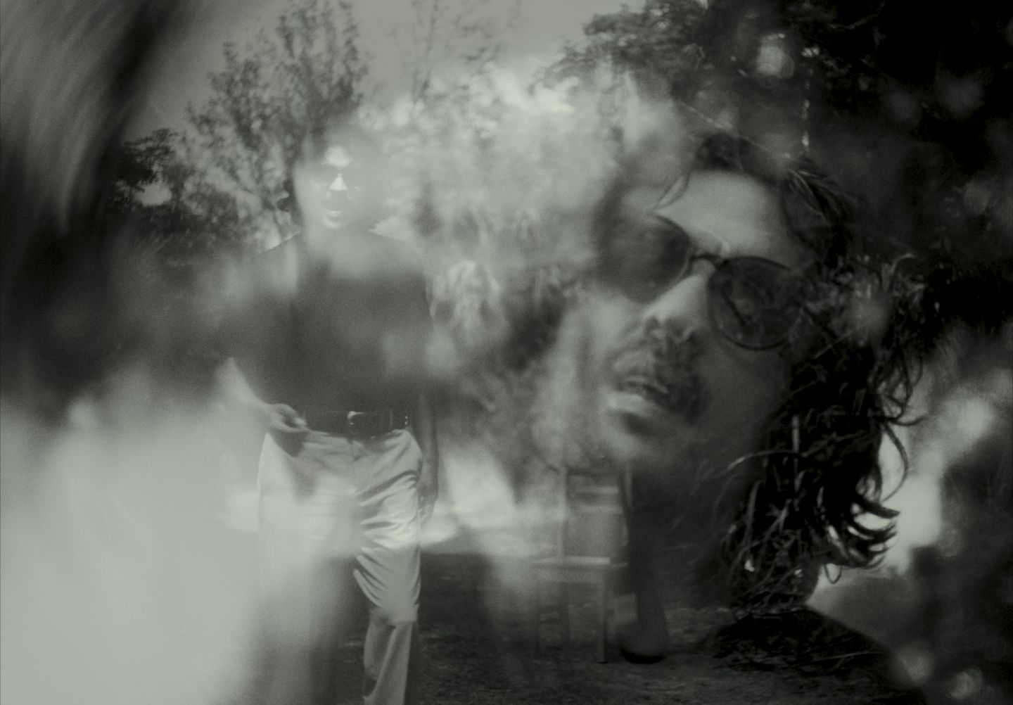 Doble exposición en blanco y negro: dos figuras superpuestas entre ramas.