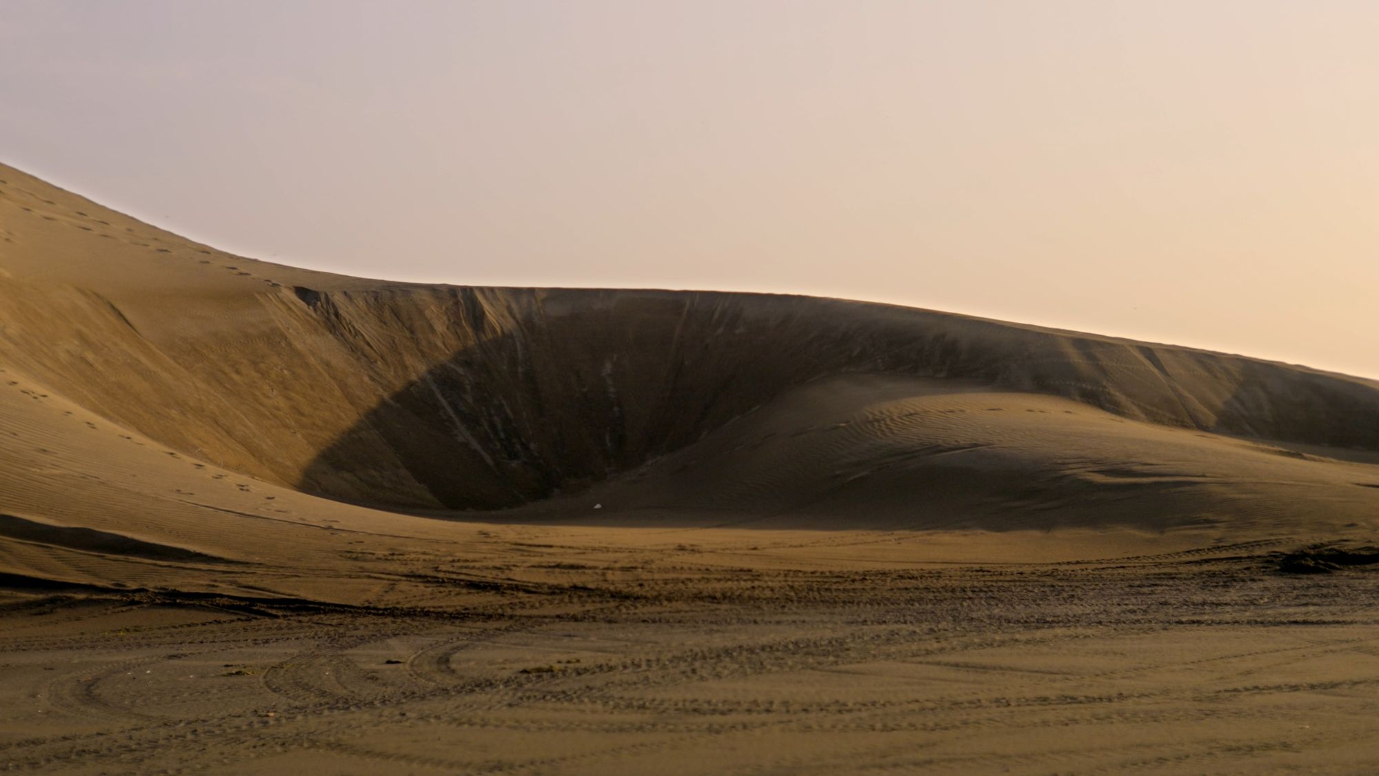 Cresta de una duna a contraluz; la arena dibuja una curva de luz ocre.
