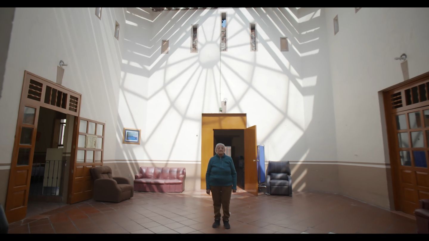 Una figura pequeña cruza una sala blanca enorme bajo un tragaluz radial.