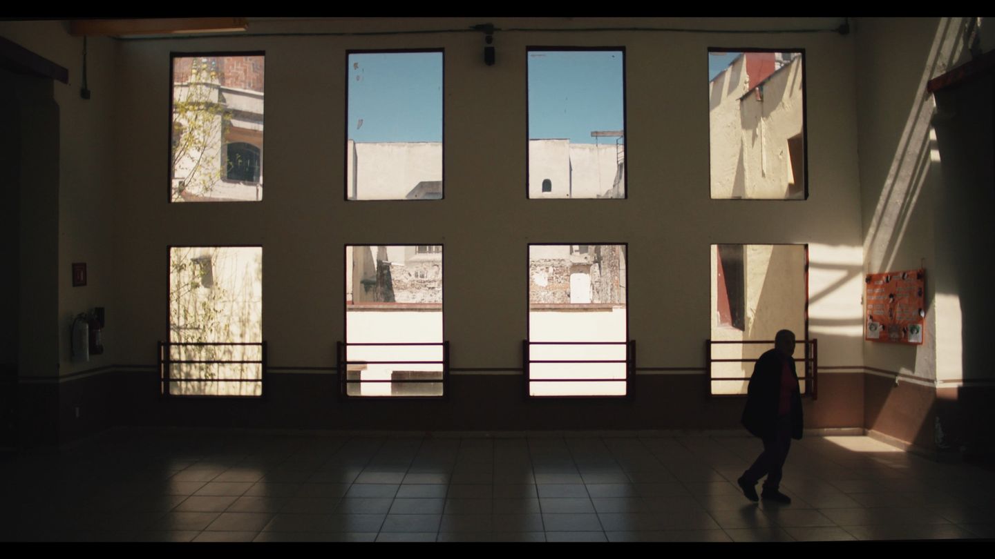 Galería interior con una hilera de ventanas; una figura la atraviesa a lo lejos.