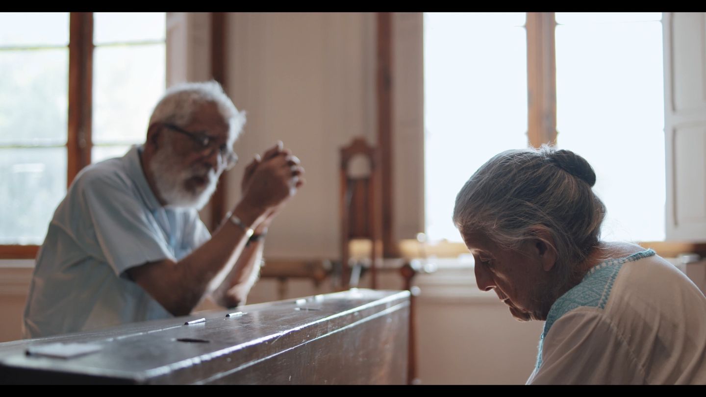 Dos personas sentadas a una mesa de madera junto a la ventana.