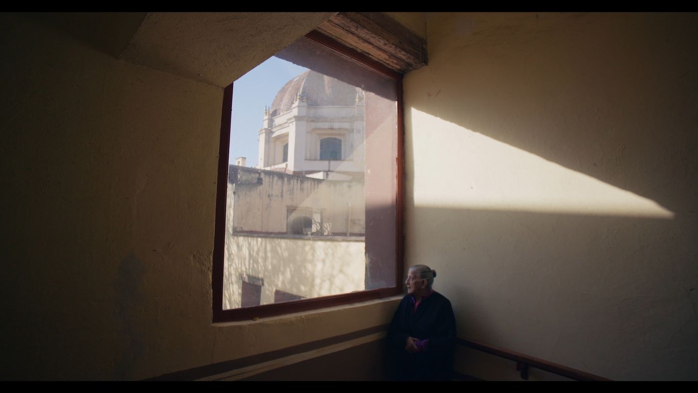 Una ventana enmarca la cúpula de una iglesia; abajo, una figura sentada.