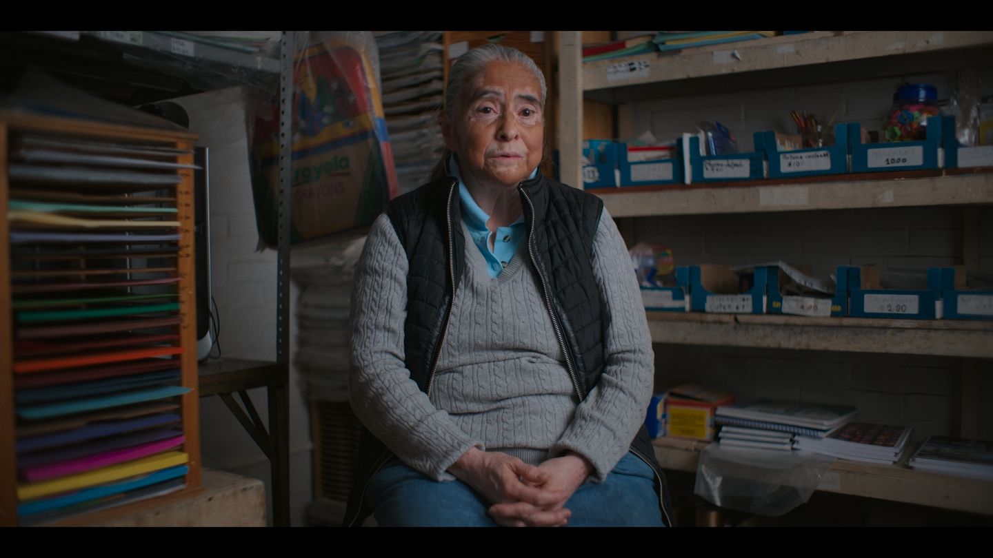 Una mujer posa sentada en su taller, rodeada de carretes de hilo de colores.