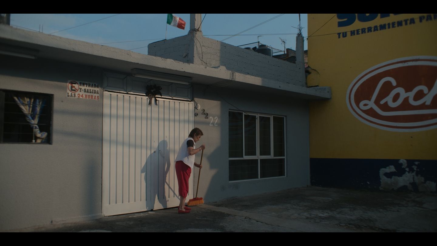 Calle de barrio: una niña de rojo junto a la reja blanca de una tienda.