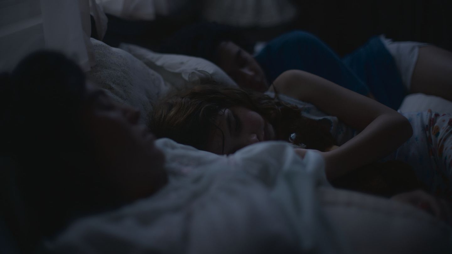 Cuerpos dormidos sobre una cama en penumbra.