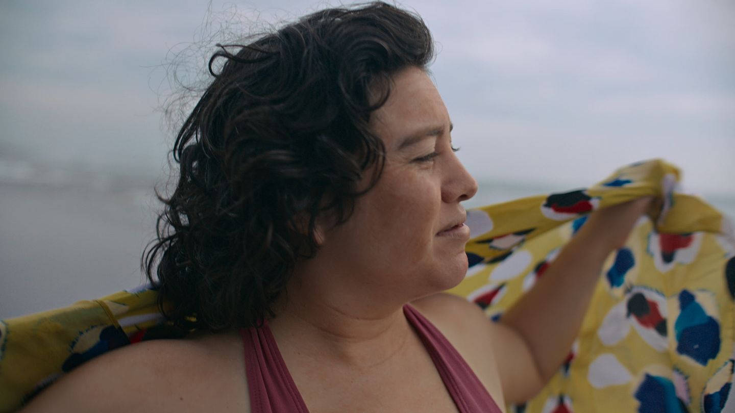 Una mujer extiende una tela estampada frente al mar.