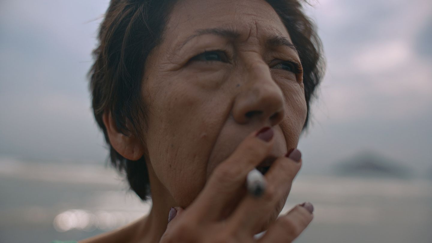 Retrato de una mujer mayor fumando, con luz de playa al atardecer.