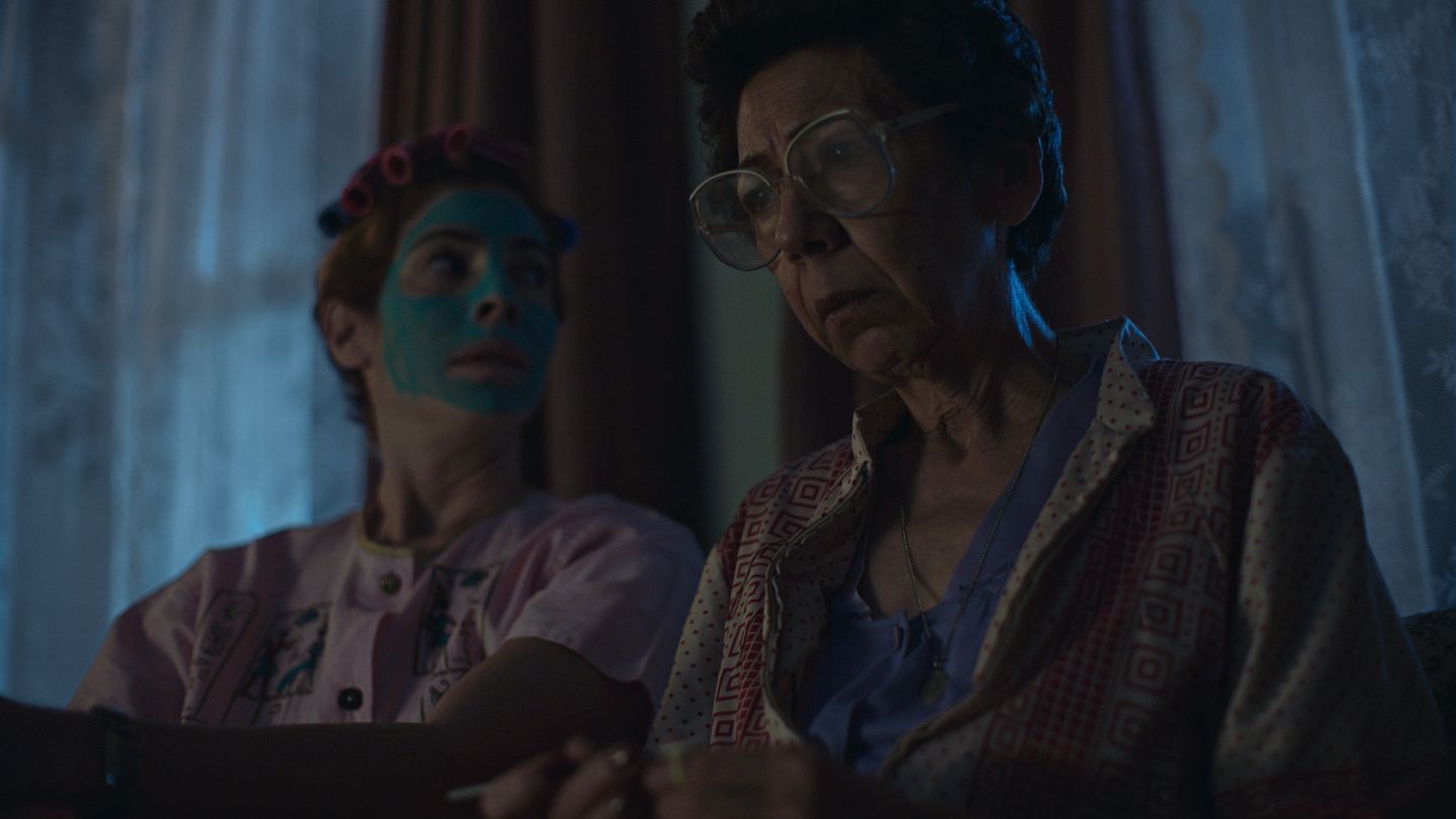 Dos mujeres en un interior bañado por luz azul de noche.